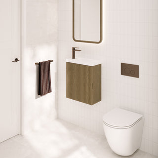 Modern bathroom vanity setup with a white wall-mounted sink cabinet, dark bronze faucet and flush plate, a tall rectangular mirror with warm lighting, a white toilet, and a dark striped towel on a white tiled wall.