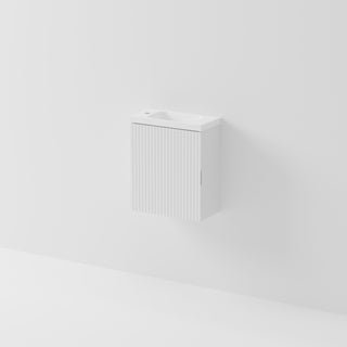 A minimalist white wall-mounted bathroom vanity cabinet with a ribbed door and an integrated sink basin, shown against a clean white wall.