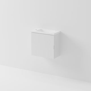 A minimalist white wall-mounted vanity cabinet with a ribbed front door and a small integrated sink, shown against a clean white wall.