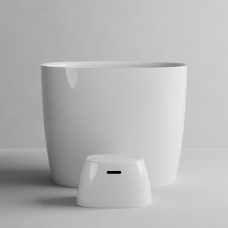 A minimalist white ceramic planter pot with a matching small white cylindrical controller or sensor placed in front of it, set against a clean light gray studio background.