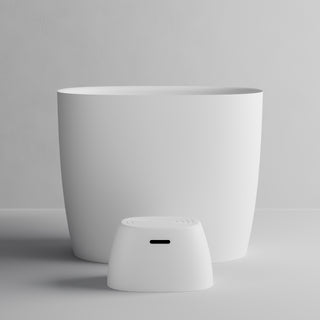 A minimalist white electronic device with a small dome-shaped front panel and a large cylindrical body, photographed on a clean light gray studio background.